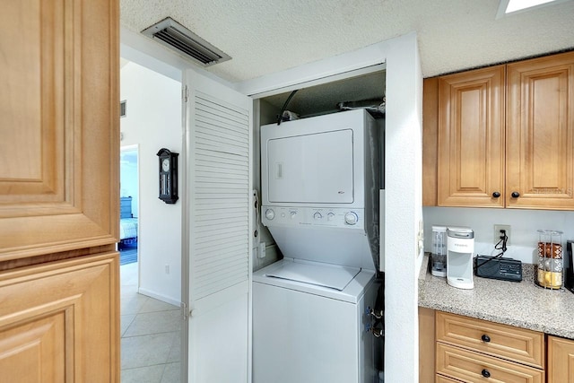 laundry room with light tile patterned floors, a textured ceiling, and stacked washing maching and dryer