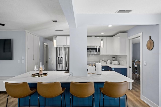 kitchen with a kitchen island, pendant lighting, white cabinetry, stainless steel appliances, and light hardwood / wood-style flooring