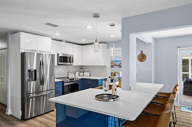 kitchen with blue cabinetry, appliances with stainless steel finishes, a center island, white cabinets, and decorative light fixtures