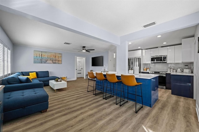 kitchen featuring a kitchen island, a breakfast bar, white cabinetry, hanging light fixtures, and stainless steel appliances