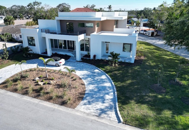 contemporary house with a front lawn, a balcony, and stucco siding