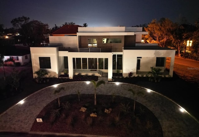 back of house at night with a balcony and stucco siding