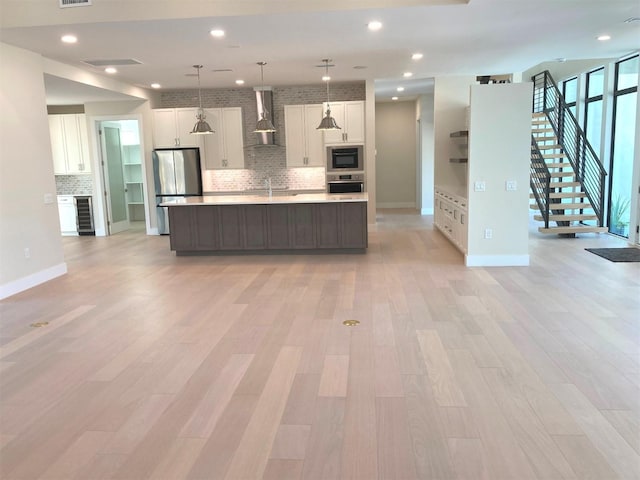 kitchen featuring pendant lighting, appliances with stainless steel finishes, wall chimney exhaust hood, and a large island