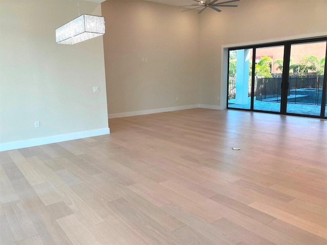 unfurnished room featuring ceiling fan with notable chandelier, light hardwood / wood-style floors, french doors, and a high ceiling