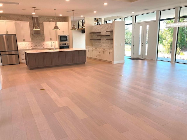 kitchen with pendant lighting, wall chimney range hood, sink, appliances with stainless steel finishes, and an island with sink