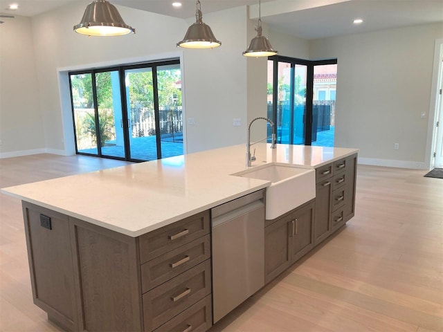 kitchen featuring sink, dishwasher, hanging light fixtures, light stone counters, and an island with sink