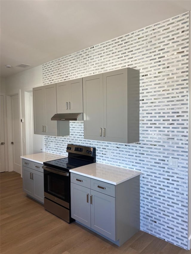 kitchen with under cabinet range hood, light countertops, stainless steel electric range, gray cabinets, and light wood finished floors