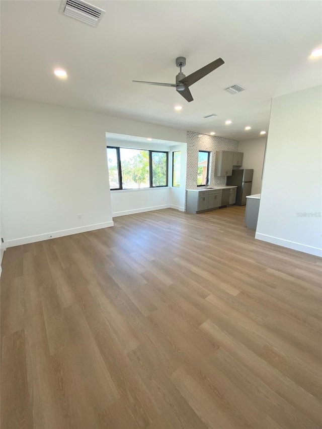 unfurnished living room with light wood-style flooring, visible vents, and baseboards