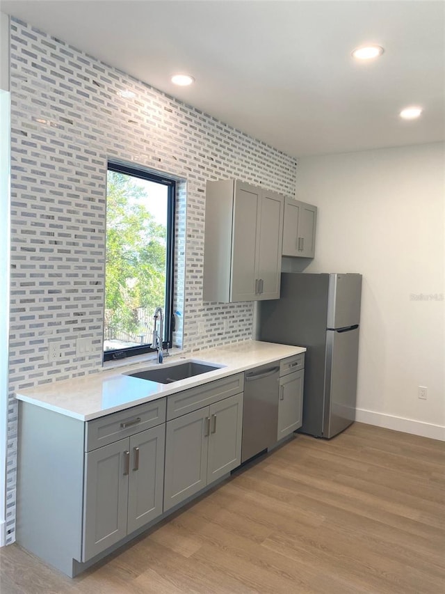 kitchen featuring light wood-style flooring, gray cabinetry, a sink, light countertops, and appliances with stainless steel finishes