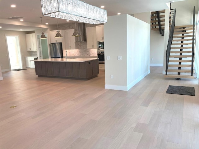 kitchen with stainless steel appliances, light countertops, a center island, wall chimney exhaust hood, and decorative light fixtures