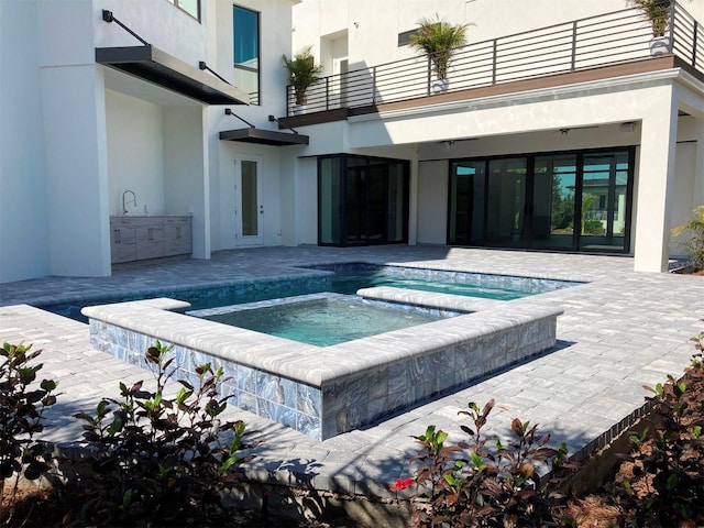 view of swimming pool featuring an in ground hot tub, a patio, an outdoor kitchen, and a sink