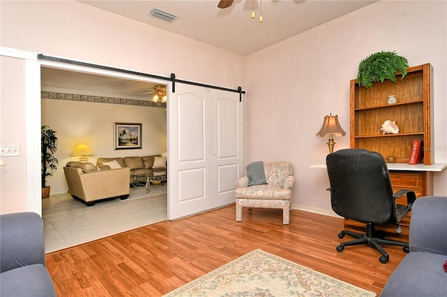 office space with ceiling fan, a barn door, and light wood-type flooring