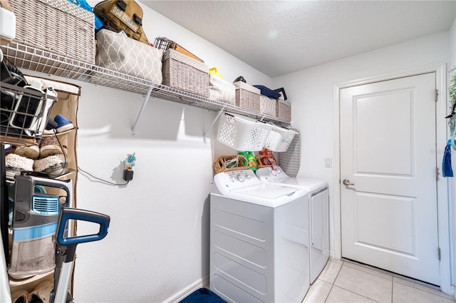 clothes washing area featuring washer and clothes dryer, a textured ceiling, and light tile patterned floors