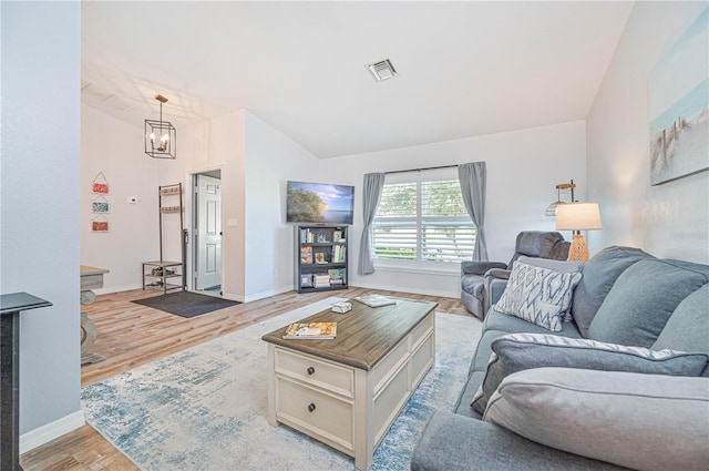 living room featuring lofted ceiling, a chandelier, and light hardwood / wood-style flooring