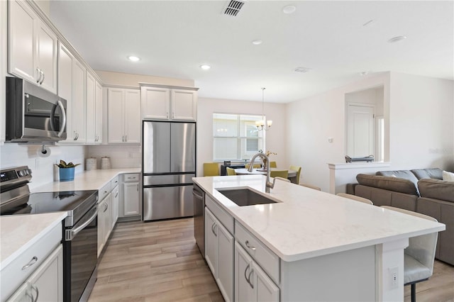 kitchen with appliances with stainless steel finishes, decorative light fixtures, sink, white cabinets, and light hardwood / wood-style flooring