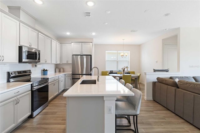 kitchen featuring sink, tasteful backsplash, decorative light fixtures, appliances with stainless steel finishes, and an island with sink