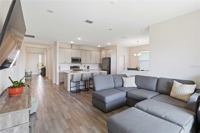 living room featuring a notable chandelier, a wealth of natural light, sink, and light wood-type flooring