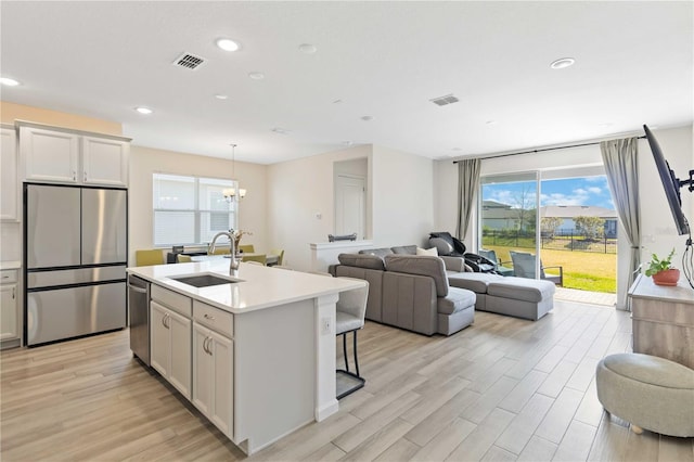 kitchen with sink, a center island with sink, light wood-type flooring, stainless steel appliances, and white cabinets