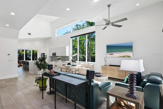 living room featuring ceiling fan, a towering ceiling, sink, and light tile patterned floors