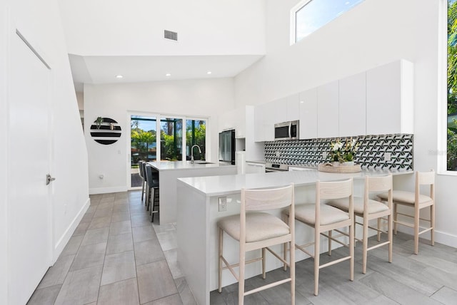 kitchen with a kitchen bar, sink, white cabinets, decorative backsplash, and a high ceiling