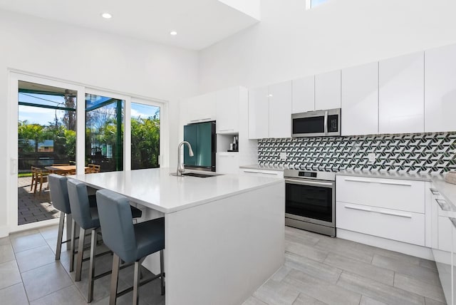 kitchen featuring a kitchen bar, tasteful backsplash, an island with sink, stainless steel appliances, and white cabinets