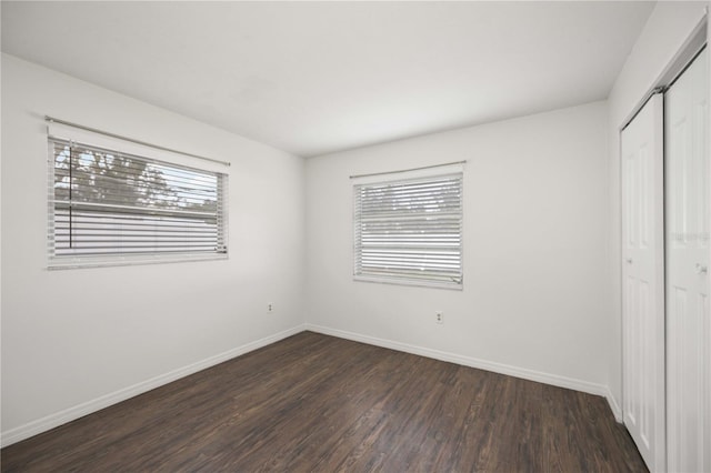 unfurnished bedroom with multiple windows, dark hardwood / wood-style floors, and a closet