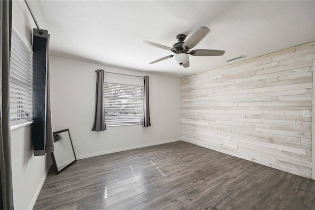 unfurnished room with ceiling fan, dark hardwood / wood-style floors, and wooden walls