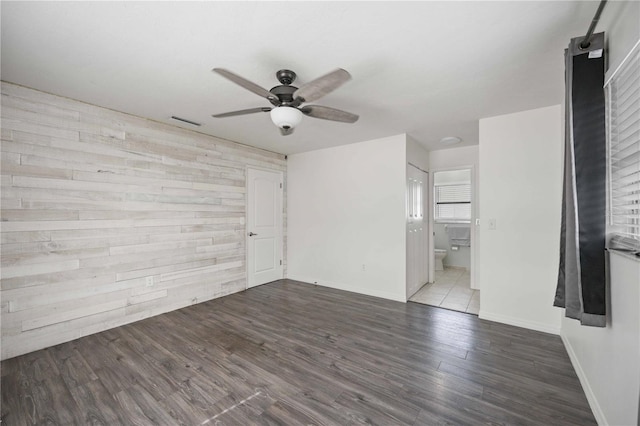 unfurnished bedroom with connected bathroom, hardwood / wood-style floors, ceiling fan, and wood walls