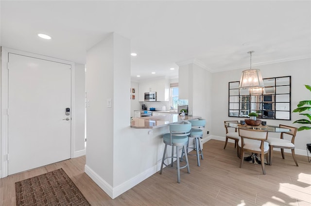 kitchen with a kitchen bar, light wood-type flooring, white cabinetry, kitchen peninsula, and hanging light fixtures