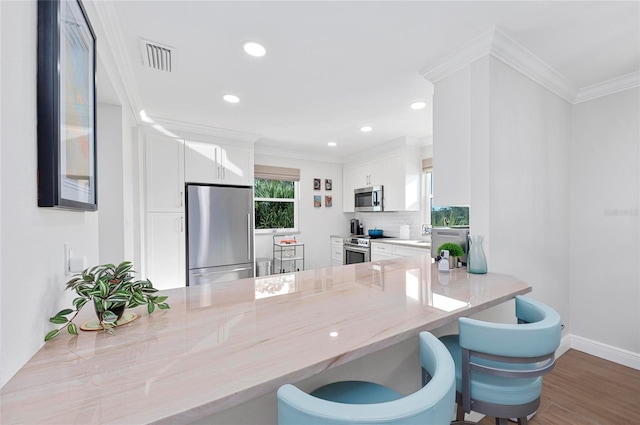 kitchen with white cabinetry, crown molding, stainless steel appliances, kitchen peninsula, and light stone countertops