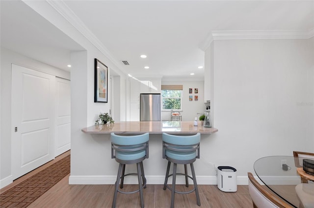 kitchen with light hardwood / wood-style flooring, crown molding, a breakfast bar, stainless steel fridge, and kitchen peninsula