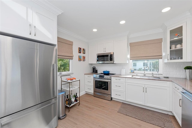 kitchen with white cabinetry, appliances with stainless steel finishes, sink, and ornamental molding