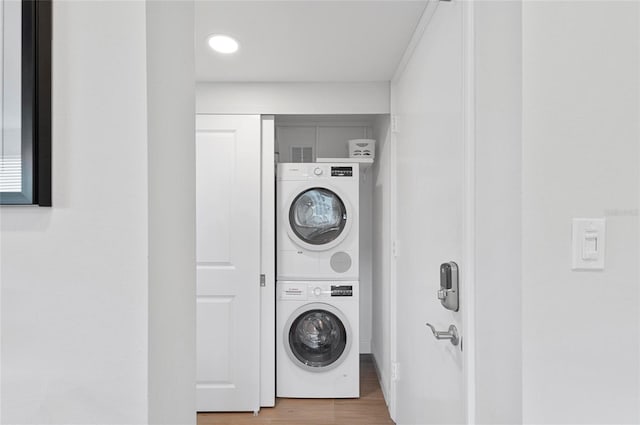 clothes washing area with hardwood / wood-style flooring and stacked washer / drying machine