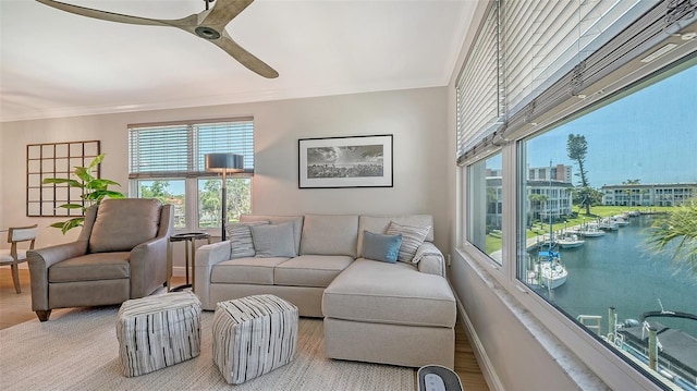 living room with wood finished floors, a water view, ceiling fan, baseboards, and ornamental molding