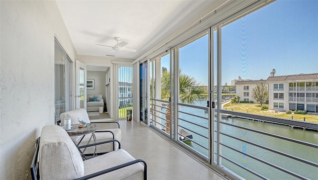 sunroom featuring ceiling fan, concrete floors, a textured wall, and a water view