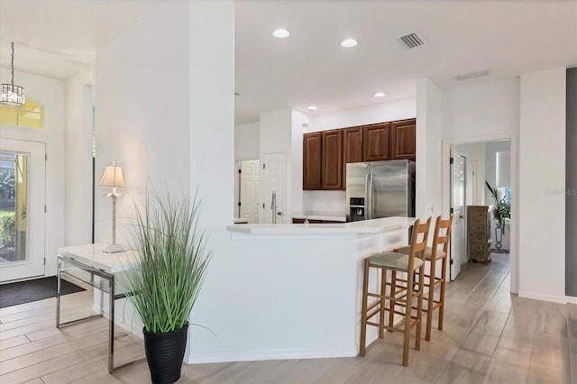 kitchen with stainless steel fridge with ice dispenser, decorative light fixtures, a breakfast bar area, light hardwood / wood-style floors, and kitchen peninsula