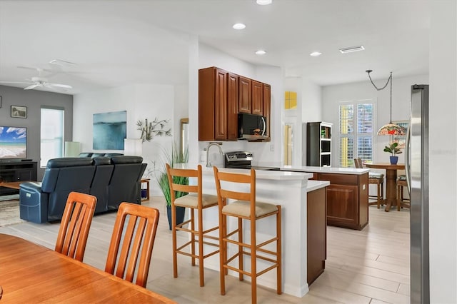 kitchen featuring a kitchen bar, kitchen peninsula, ceiling fan, stainless steel appliances, and light hardwood / wood-style floors