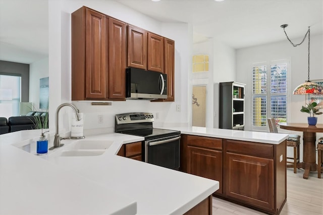 kitchen with sink, light wood-type flooring, appliances with stainless steel finishes, kitchen peninsula, and pendant lighting