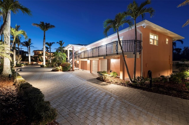 property exterior at twilight with a garage, decorative driveway, a balcony, and stucco siding