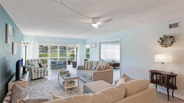 living room with a textured ceiling, visible vents, baseboards, a ceiling fan, and light wood finished floors