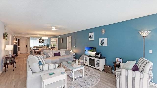 living area with light wood-style floors, ceiling fan, baseboards, and a textured ceiling