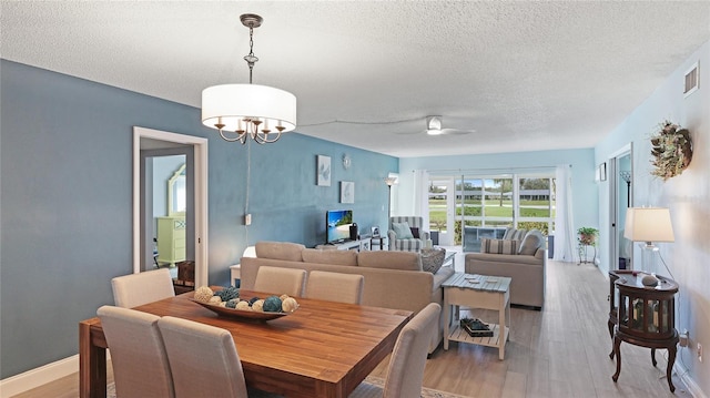 dining room with light wood-type flooring, visible vents, a textured ceiling, and ceiling fan with notable chandelier