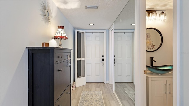 interior space featuring light wood-style floors, a textured ceiling, visible vents, and a sink