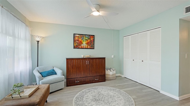 sitting room with visible vents, light wood-style floors, ceiling fan, a textured ceiling, and baseboards