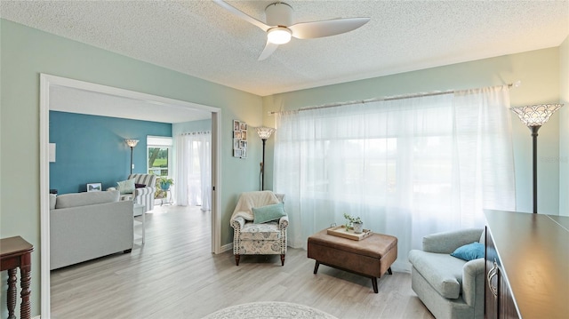 living area with ceiling fan, light hardwood / wood-style flooring, and a textured ceiling