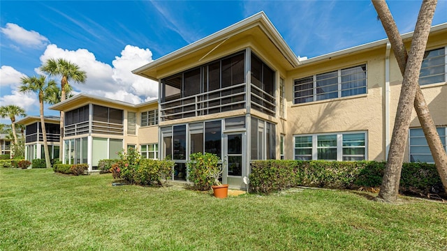 back of house with a sunroom, a lawn, and stucco siding