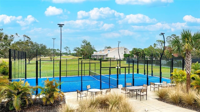 view of sport court featuring a tennis court, fence, and a yard