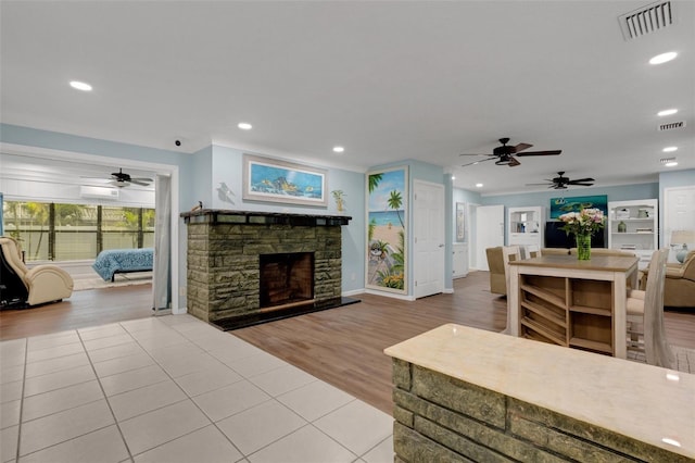 living room with ceiling fan, a wall mounted air conditioner, a stone fireplace, and light wood-type flooring