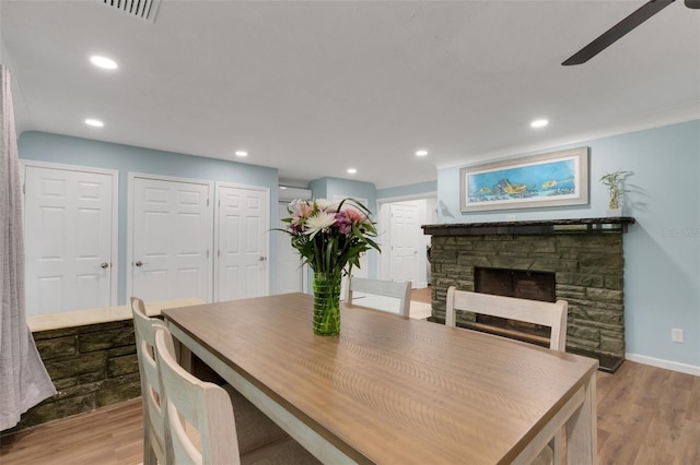 dining space with ceiling fan, a stone fireplace, and light hardwood / wood-style floors