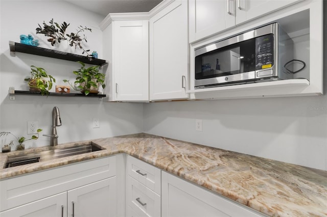 kitchen with light stone counters, sink, and white cabinets